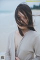 A woman standing on a beach with her hair blowing in the wind.