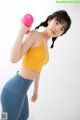 A woman in a yellow top and blue leggings holding a pink dumbbell.