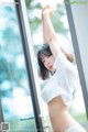 A woman in a white shirt is posing by a window.