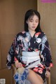 A woman in a kimono sitting on a chair holding a fan.