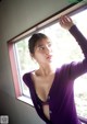 A woman in a purple cardigan leaning against a window.