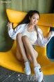 A woman sitting on a yellow chair wearing white sneakers.