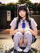 A girl in a school uniform sitting on the ground.