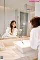 A woman in a white robe looking at herself in the mirror.