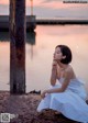 A woman in a white dress sitting on a rock by the water.