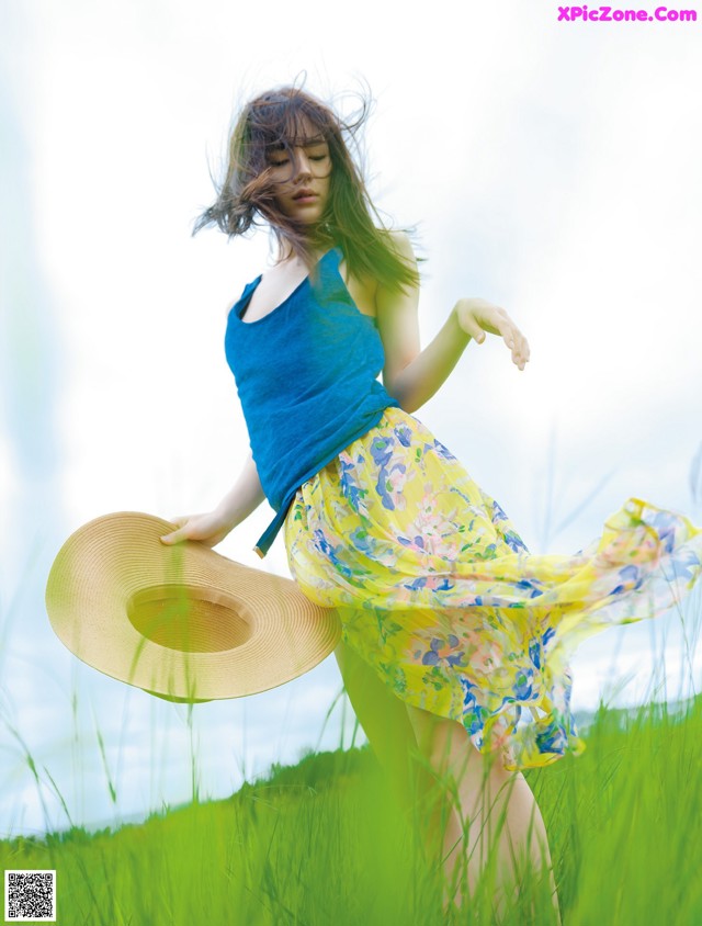A woman in a blue tank top and yellow skirt is dancing in a field.